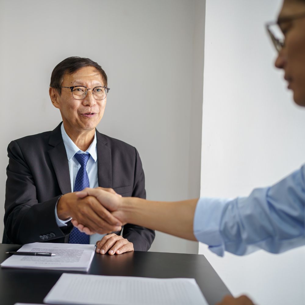 Smiling lawyer wearing glasses shaking hands with another person across a desk during a meeting