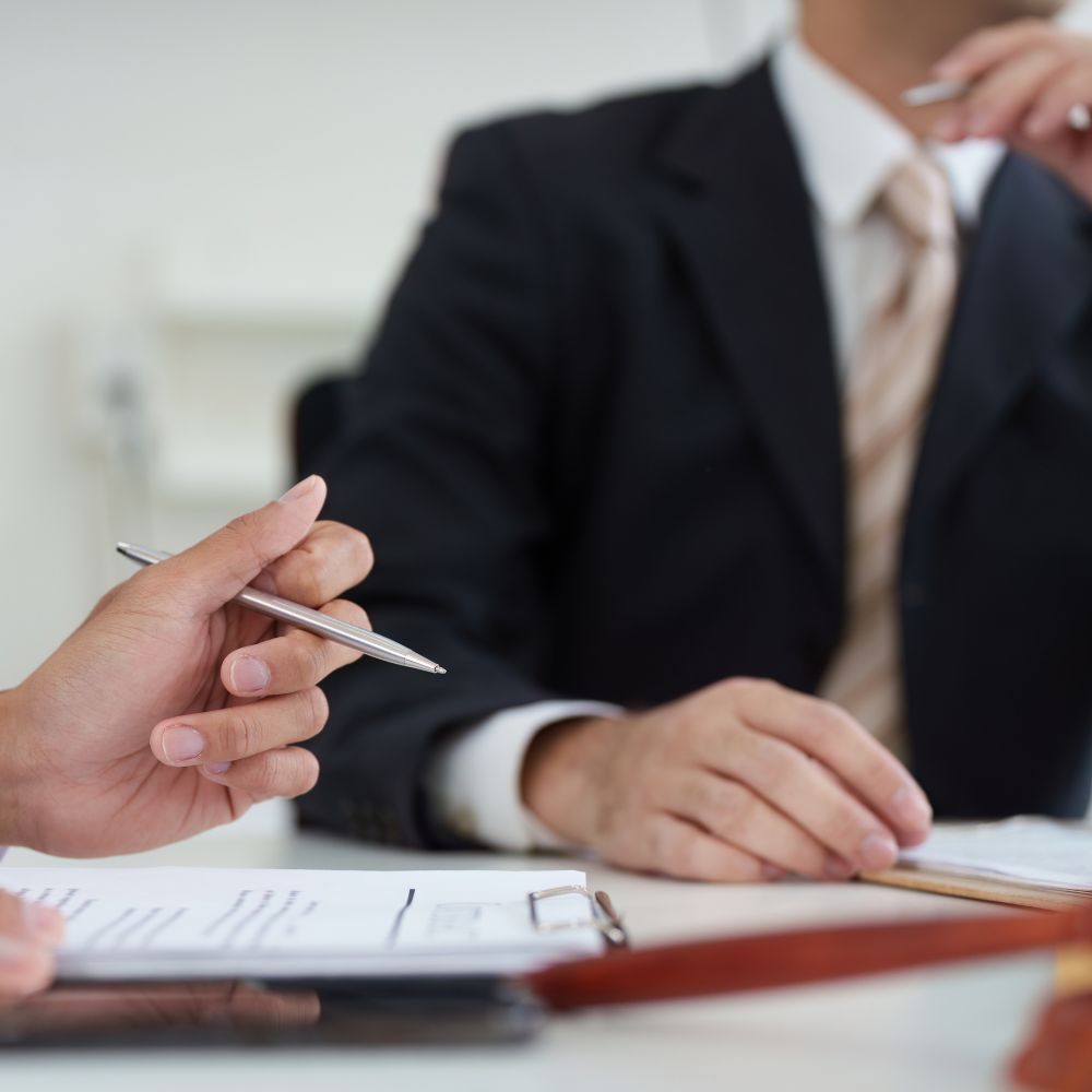 Close-up of two people holding pens and reviewing a legal document on a clipboard