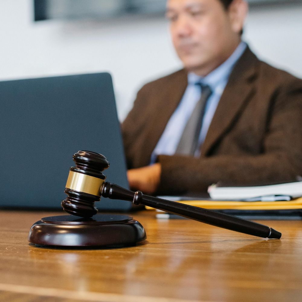 Judge’s gavel in focus on a desk, with a lawyer in a suit working on a laptop in the background