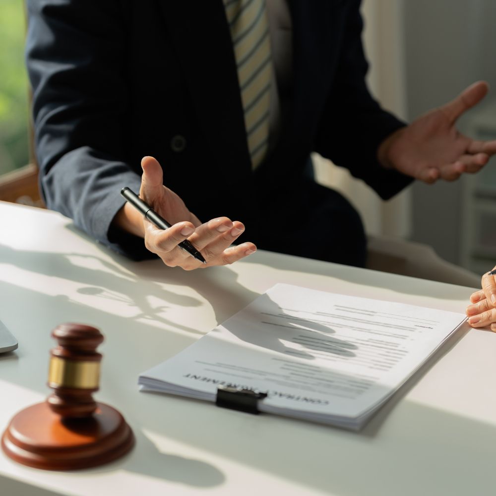 An attorney gesturing while discussing a contract document on a desk with a gavel nearby
