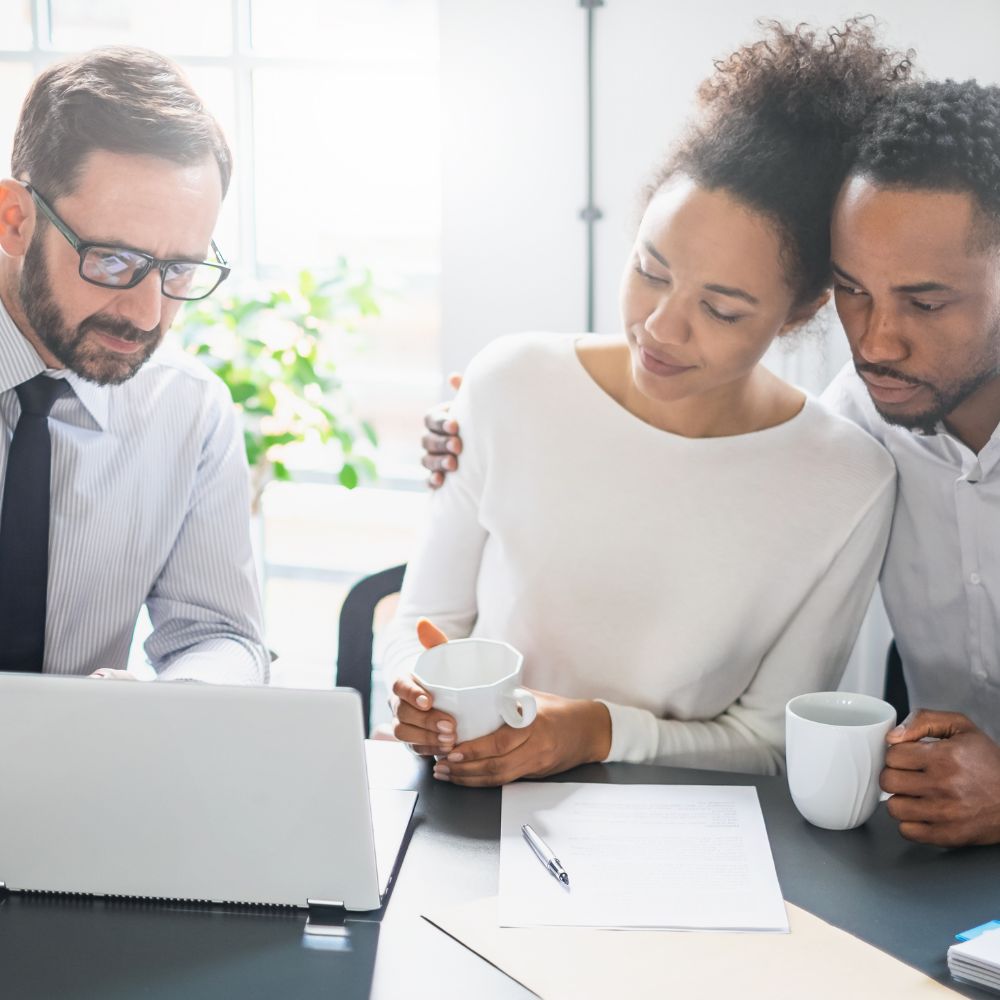 Couple meeting with a lawyer, reviewing documents on a desk with a laptop and coffee mugs