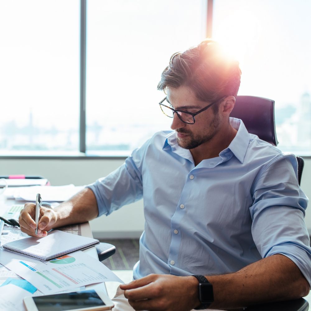 A businessman light blue shirt working at his desk with documents, charts, and a smartphone