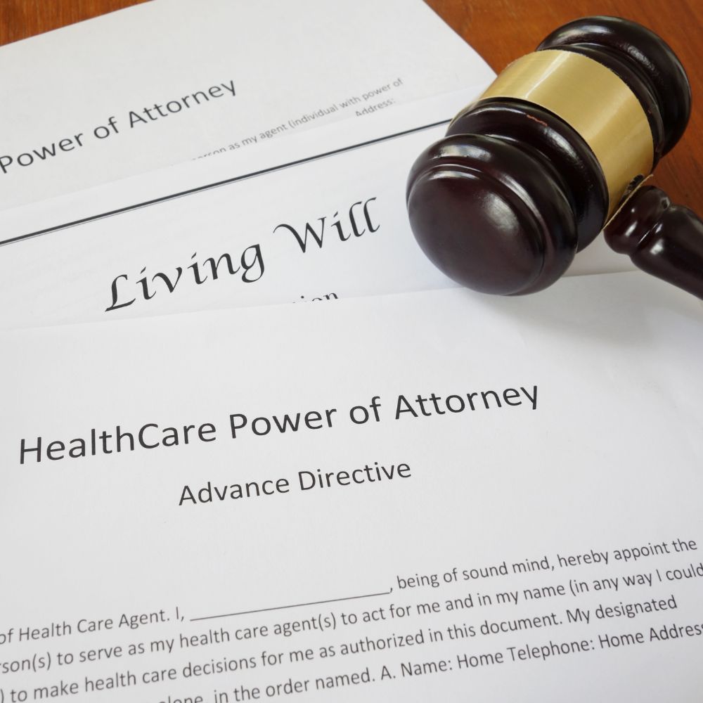 Close-up of legal documents titled “HealthCare Power of Attorney,” “Living Will,” and “Power of Attorney,” next to a judge’s gavel