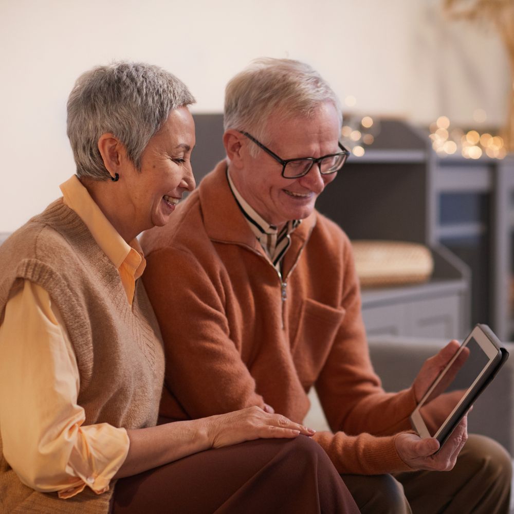 Happy older couple sitting together and smiling while looking at a digital tablet