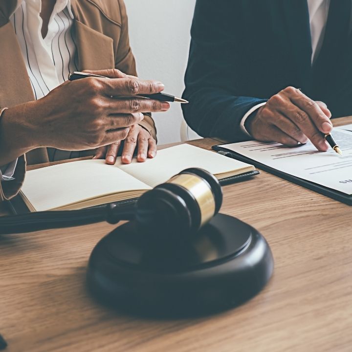 A lawyer and a client sitting across from each other at a desk with a gavel and documents