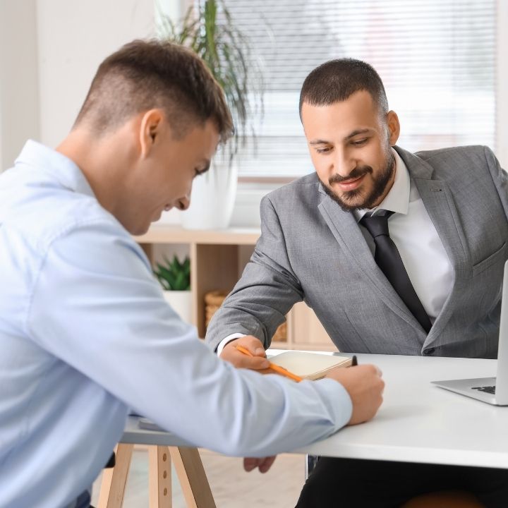 A lawyer and a client at a desk with one person holding a pen and the other is signing a document