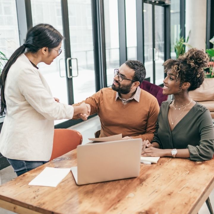 A lawyer and a man shaking hands with his partner beside him, completing a legal meeting or agreement