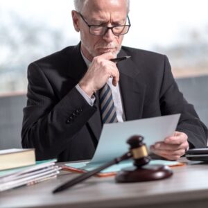 Attorney reading document at desk with gavel and legal files visible.